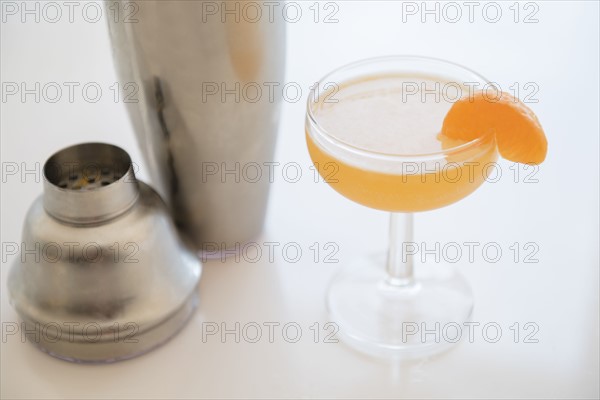 Cocktail in drinking glass and cocktail shaker on table