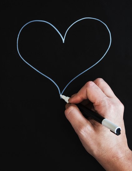 Man's hand drawing heart shape on black paper