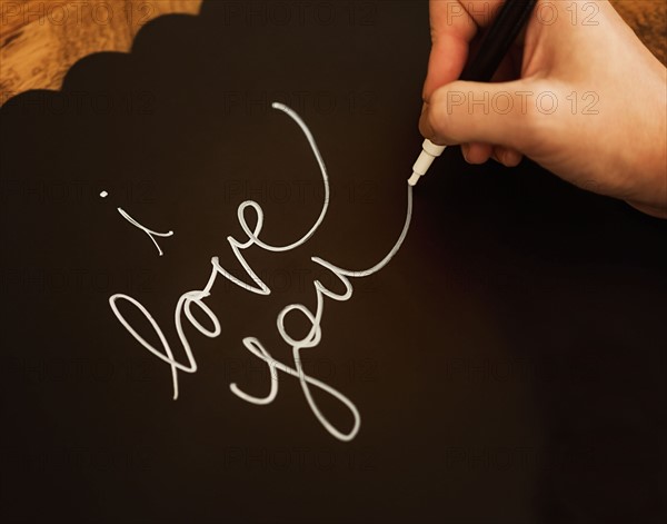 Man's hand writing I Love You on black paper