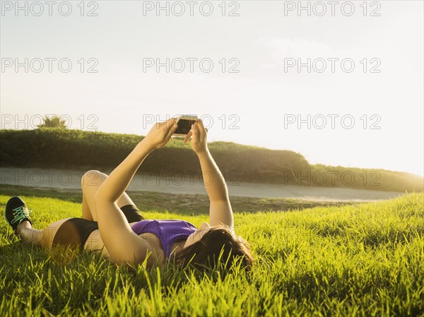 Young woman lying on grass using phone