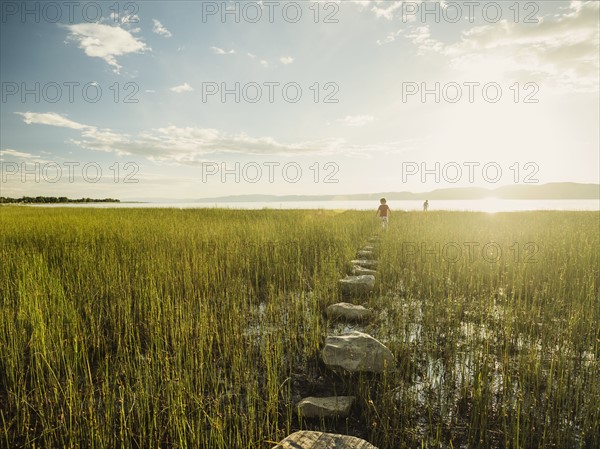 Small girl and boy (4-5) walking on stepping stones in meadow