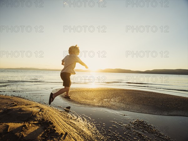 Small boy (4-5) jumping over water on sunny day