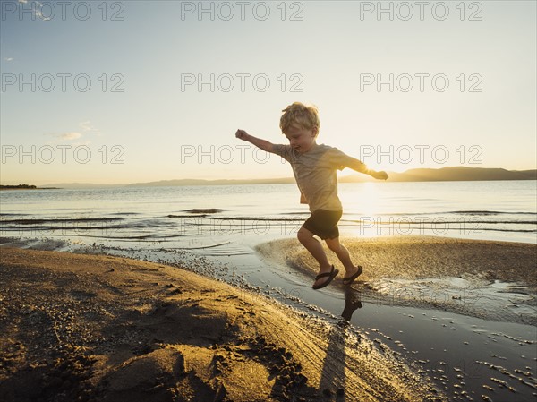 Small boy (4-5) jumping over water on sunny day