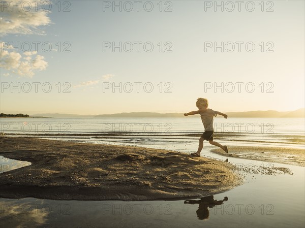 Small boy (4-5) jumping over water on sunny day