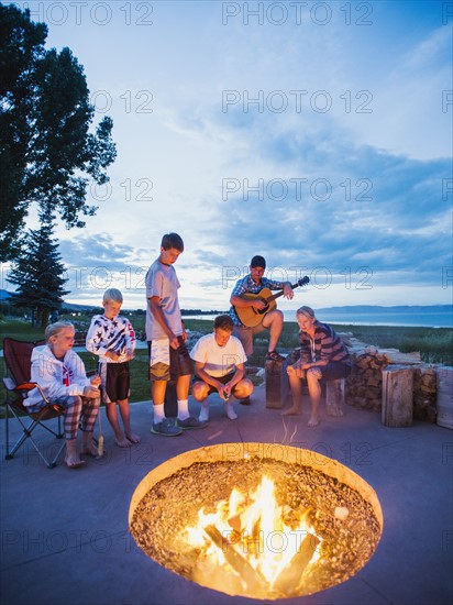 Parents with children (8-9, 10-11, 16-17) sitting in front of campfire and playing guitar