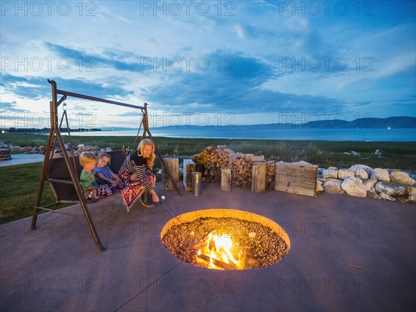 Mother with children (4-5) sitting on wooden swing in front of campfire