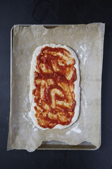 Pizza dough with tomato sauce on wax paper