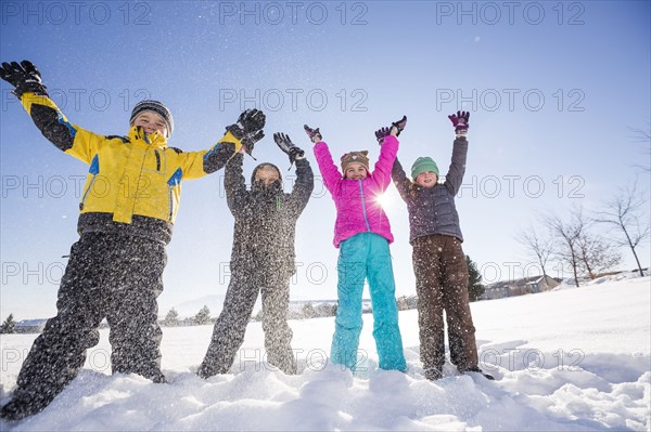 Children (8-9, 10-11) standing in snow with arms raised