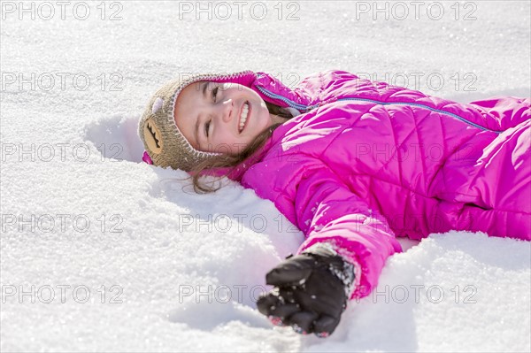Girl (10-11) in pink jacket lying in snow