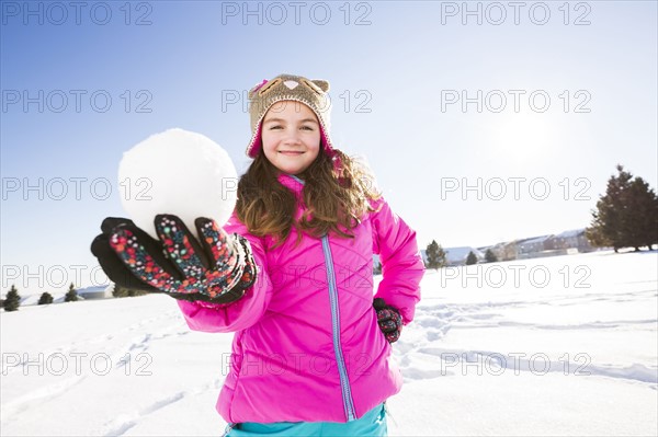 Girl (10-11) in pink jacket holding snowball