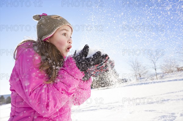 Girl (10-11) in pink jacket blowing snow