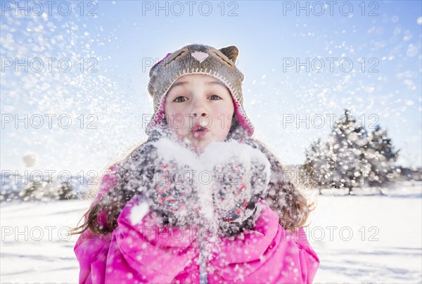 Girl (10-11) in pink jacket blowing snow