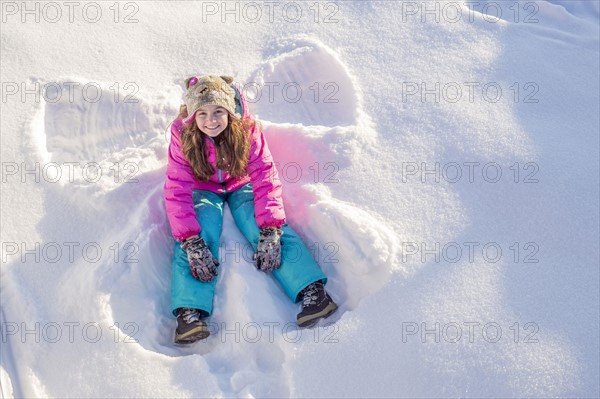 Girl (10-11) in pink jacket sitting in snow