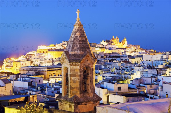 Illuminated townscape with church tower in foreground at dusk