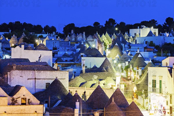 Trulli houses along illuminated street under blue sky