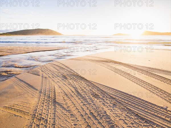 Tire tracks on beach at sunset