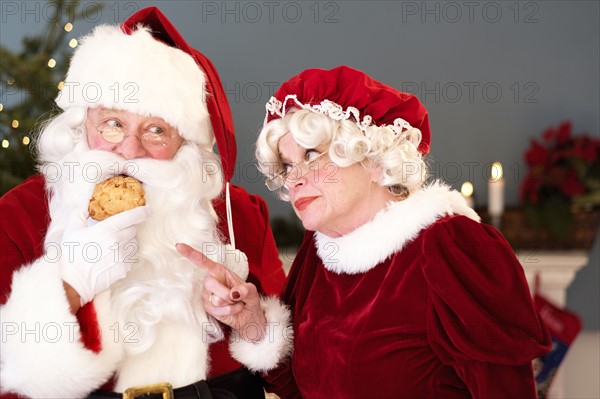 Mrs. Claus pointing on Santa eating gingerbread cookie.