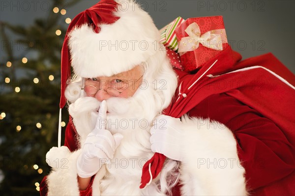 Portrait of Santa Claus with finger on lips, carrying sack over shoulder.