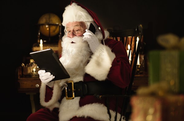 Santa Claus using digital tablet and talking by mobile phone.