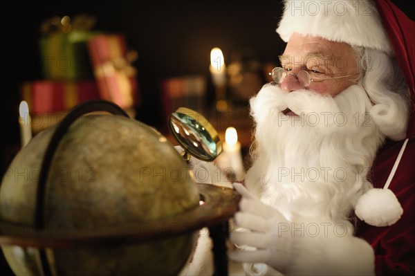 Santa Claus looking through magnifying glass at globe.