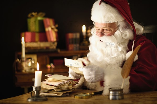 Portrait of Santa Claus reading child's letter at desk.