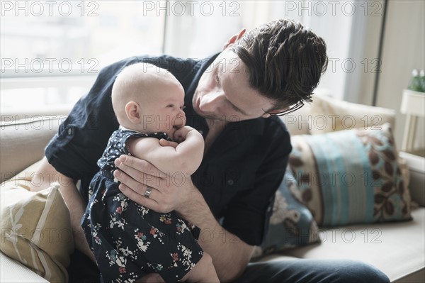 Father sitting on sofa and playing with baby daughter (2-5 months).