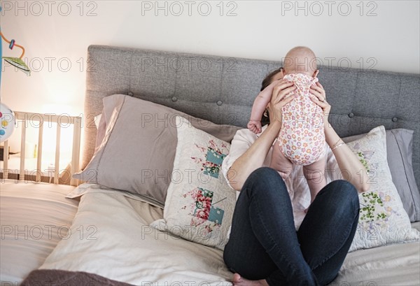 Mother playing with baby daughter (2-5 months) in bedroom.