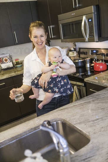 Smiling mother holding baby daughter (2-5 months) and glass of water.