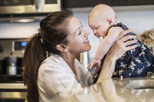 Mother playing with baby daughter (2-5 months) in kitchen.