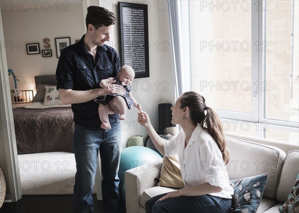 Parents playing with baby daughter (2-5 months) in living room.