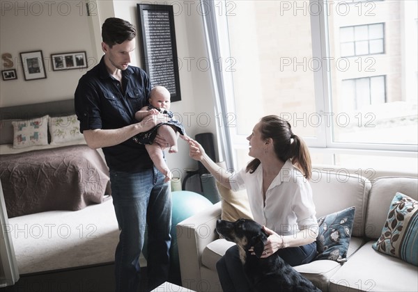 Parents playing with baby daughter (2-5 months) and dog in living room.