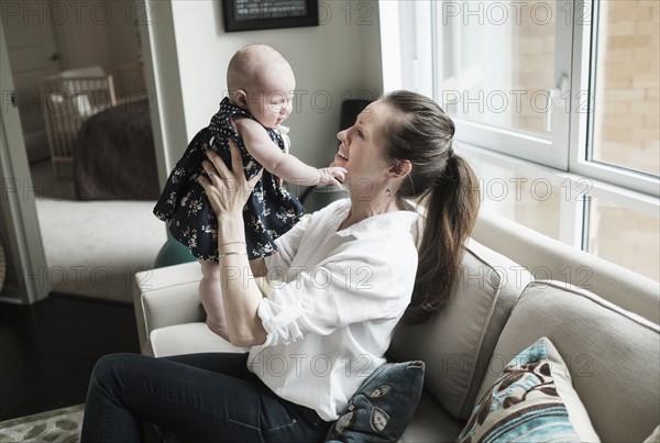 Mother playing with baby daughter (2-5 months) in living room.