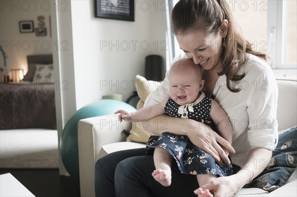 Mother sitting on sofa with crying baby daughter (2-5 months) in living room.