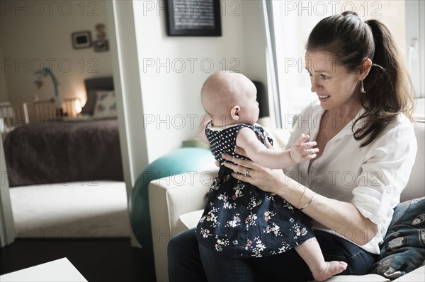 Mother playing with baby daughter (2-5 months) in living room.