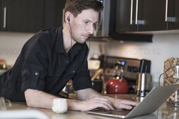 Man working on laptop computer in kitchen.