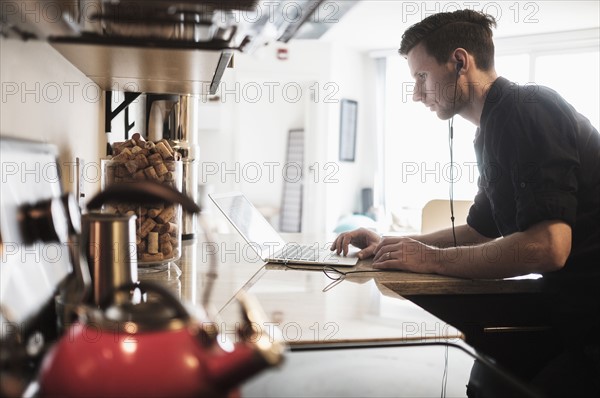 Man working on laptop computer in kitchen.