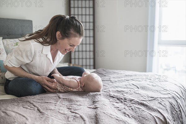 Mother playing with baby daughter (2-5 months) in bedroom.
