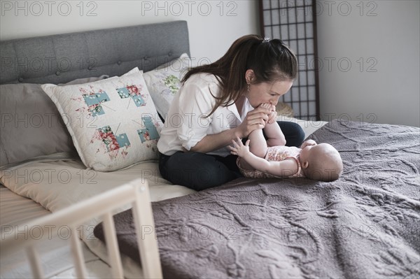Mother kissing baby daughter's (2-5 month) feet in bedroom.