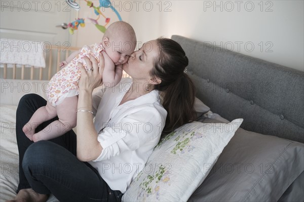 Mother kissing baby daughter (2-5 months) in bedroom.