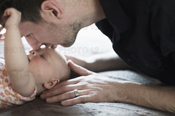 Father playing with daughter (2-5 months) on bed.