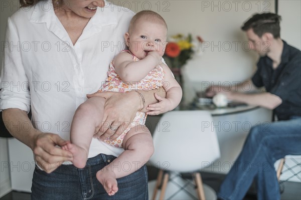 Mother holding baby (2-5 months) and father working in background.