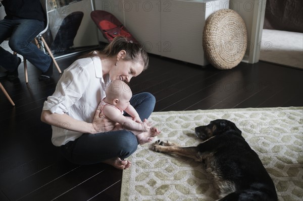 Mother holding baby (2-5 months) and playing with dog.