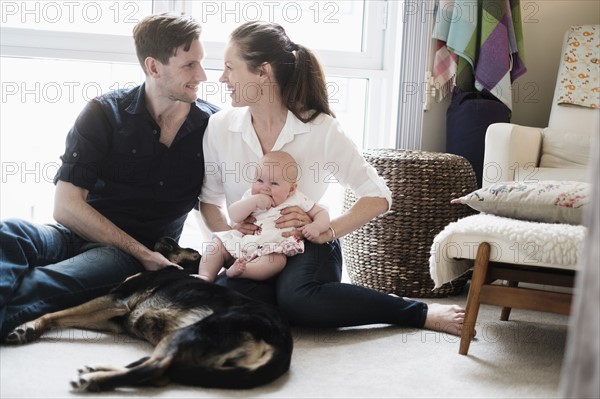 Portrait of happy family sitting on carpet with daughter (2-5 months) and dog.