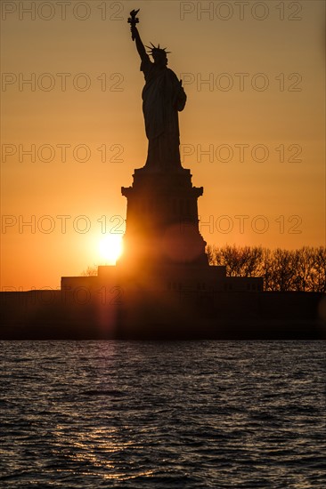 Silhouette of Statue of Liberty at sunset. USA, New York, New York City.