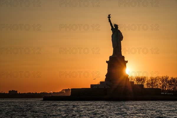 Silhouette of Statue of Liberty at sunset. USA, New York, New York City.