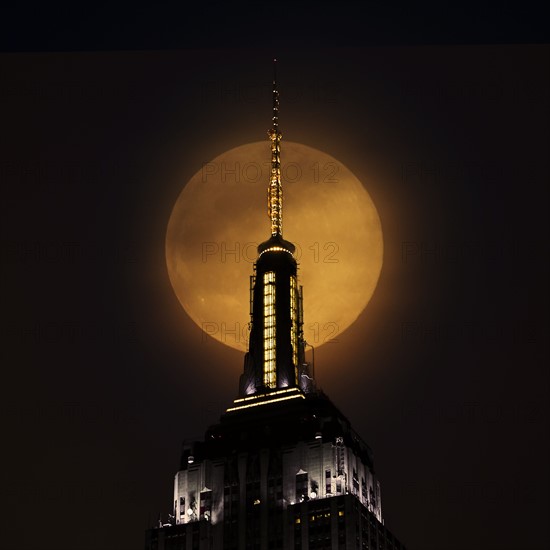 Spire of Empire State Building with full moon in background. USA, New York, New York City.