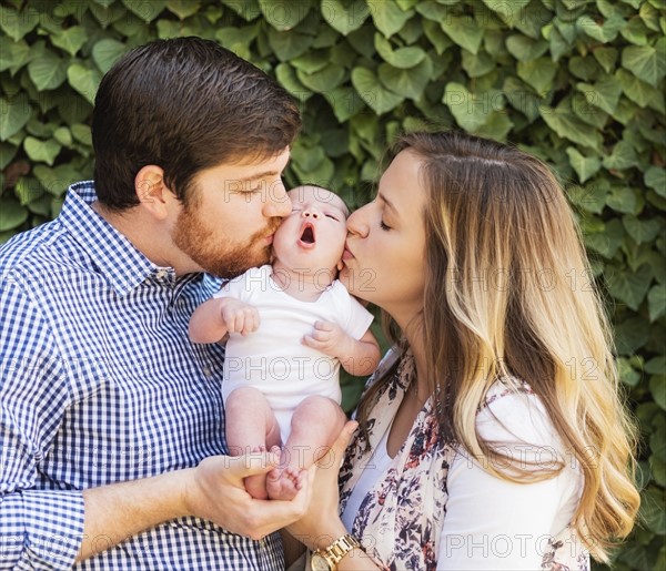 Happy parents kissing girl (2-5 months)