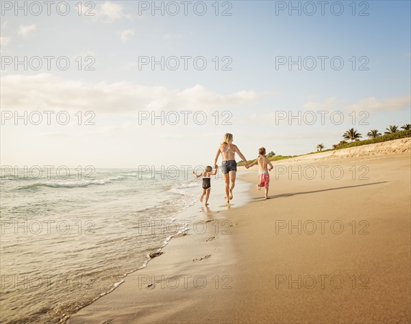 Mother running with boy (6-7) and girl (4-5) on beach by water