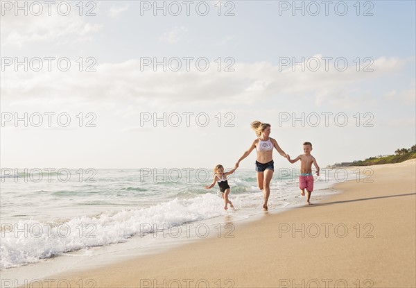 Mother running with boy (6-7) and girl (4-5) on beach by water