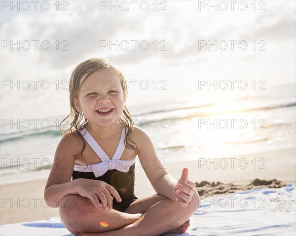 Girl (4-5) sitting cross- legged on beach